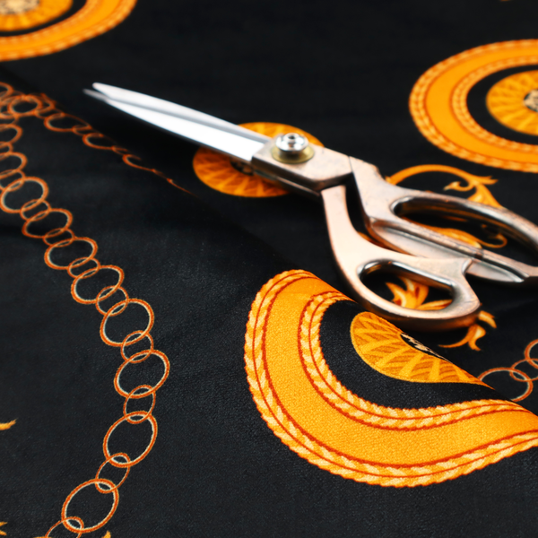 A luxury baroque-style fabric on a black ground featuring a trellis of golden chains interspersed with ornate sun-medallions and amber floral scrolls.