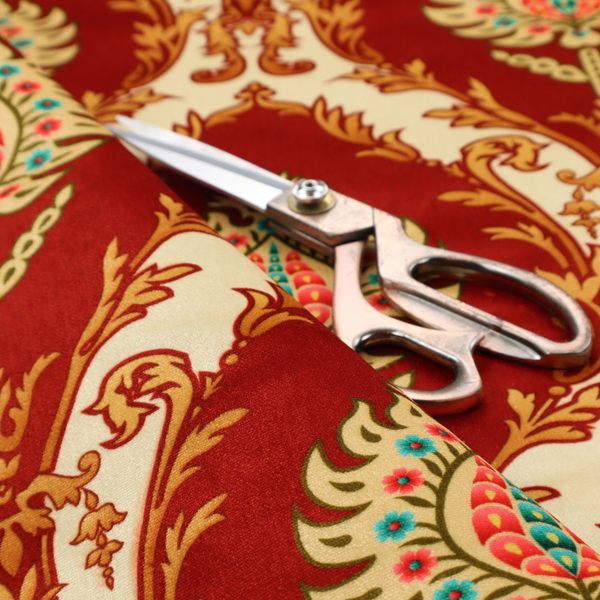 A grand, symmetrical damask-style fabric on a rich crimson red ground featuring ornate cream-colored leaf frames enclosing vibrant, stylized floral pinecones with teal and pink accents.