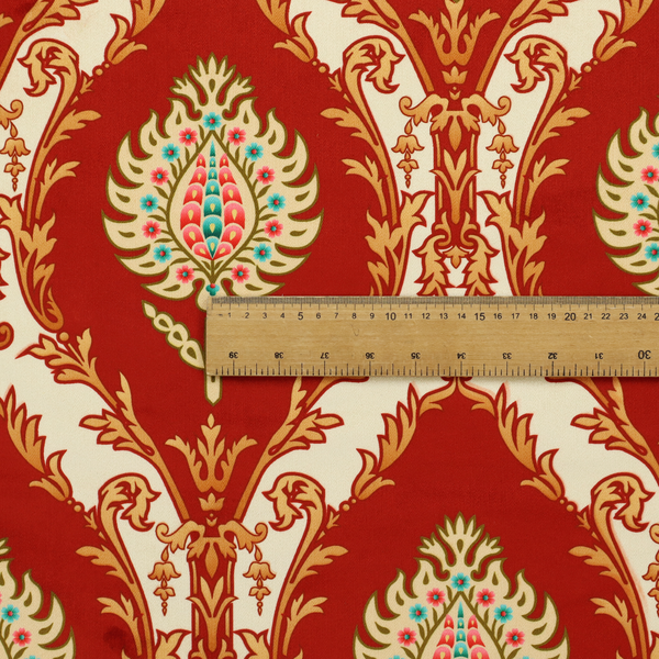 A grand, symmetrical damask-style fabric on a rich crimson red ground featuring ornate cream-colored leaf frames enclosing vibrant, stylized floral pinecones with teal and pink accents.