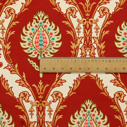A grand, symmetrical damask-style fabric on a rich crimson red ground featuring ornate cream-colored leaf frames enclosing vibrant, stylized floral pinecones with teal and pink accents.