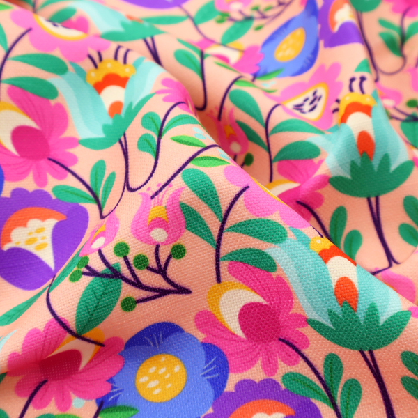 A vibrant and energetic floral fabric on a soft peach-blush background. The design features a symmetrical folk-art arrangement of stylized flowers in neon pink, electric blue, violet, and turquoise, connected by emerald green leaves and delicate black stems in a dense, mirrored repeat.