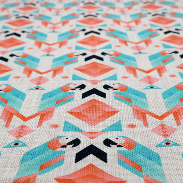 A modern and vibrant geometric fabric on a textured, off-white linen-look background. The design features a symmetrical repeat of abstract parrots rendered in sharp, angular 'prism' shapes of turquoise, coral-pink, and charcoal black. Interspersed between the birds are large coral diamonds and teal triangles, creating a balanced, contemporary tribal-pop aesthetic.