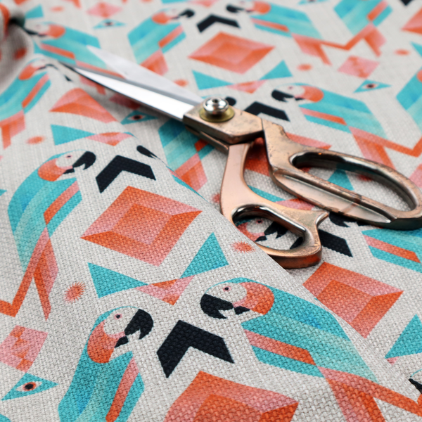 A modern and vibrant geometric fabric on a textured, off-white linen-look background. The design features a symmetrical repeat of abstract parrots rendered in sharp, angular 'prism' shapes of turquoise, coral-pink, and charcoal black. Interspersed between the birds are large coral diamonds and teal triangles, creating a balanced, contemporary tribal-pop aesthetic.