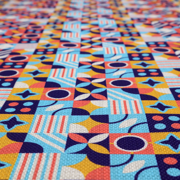 A high-energy, multi-coloured geometric fabric featuring a rhythmic grid of Bauhaus-inspired motifs. The design is a playful mosaic of circles, stars, stripes, and quarter-moons in a vibrant palette of mustard yellow, coral pink, sky blue, and deep midnight navy, all set against a textured, off-white linen-look background.