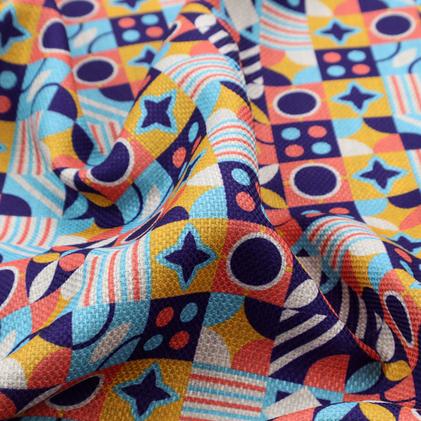 A high-energy, multi-coloured geometric fabric featuring a rhythmic grid of Bauhaus-inspired motifs. The design is a playful mosaic of circles, stars, stripes, and quarter-moons in a vibrant palette of mustard yellow, coral pink, sky blue, and deep midnight navy, all set against a textured, off-white linen-look background.