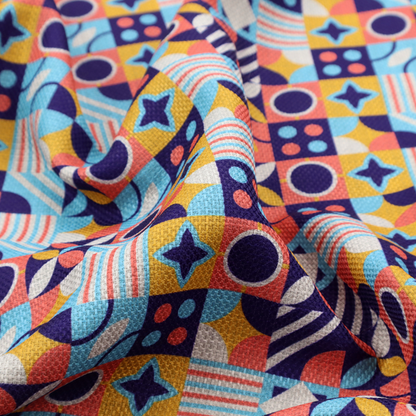 A high-energy, multi-coloured geometric fabric featuring a rhythmic grid of Bauhaus-inspired motifs. The design is a playful mosaic of circles, stars, stripes, and quarter-moons in a vibrant palette of mustard yellow, coral pink, sky blue, and deep midnight navy, all set against a textured, off-white linen-look background.