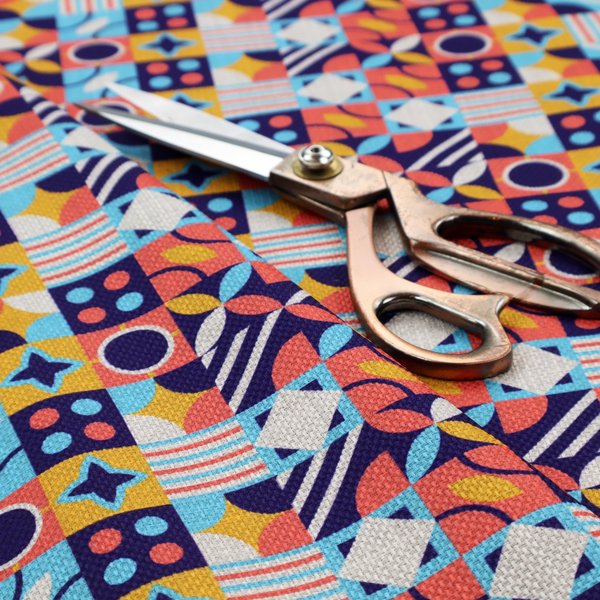 A high-energy, multi-coloured geometric fabric featuring a rhythmic grid of Bauhaus-inspired motifs. The design is a playful mosaic of circles, stars, stripes, and quarter-moons in a vibrant palette of mustard yellow, coral pink, sky blue, and deep midnight navy, all set against a textured, off-white linen-look background.