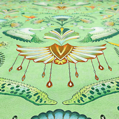 Ornate upholstery fabric with a mirrored botanical and wildlife design. Features white herons with outspread wings, crocodiles, hummingbirds, and butterflies surrounding stylized teal and gold fan motifs on a soft lime-green base.