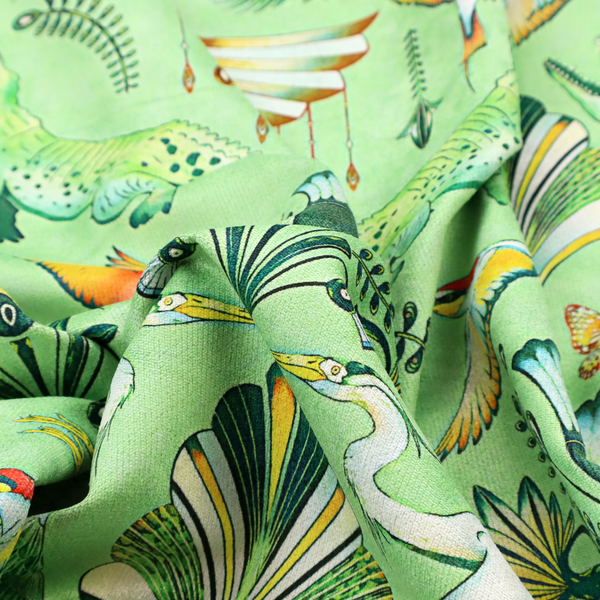 Ornate upholstery fabric with a mirrored botanical and wildlife design. Features white herons with outspread wings, crocodiles, hummingbirds, and butterflies surrounding stylized teal and gold fan motifs on a soft lime-green base.