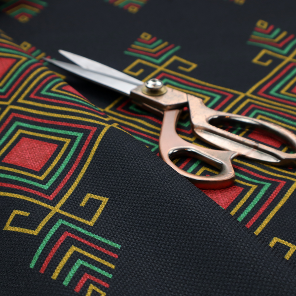 A geometric tribal pattern featuring red, yellow, and green diamonds and linear motifs on a dark charcoal-black fabric background.
