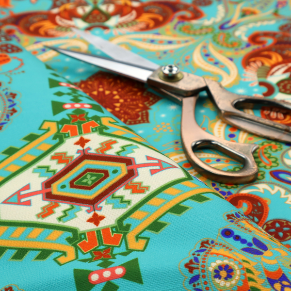 A vibrant and detailed ornamental fabric on a bright turquoise-azure background. The design features a large, symmetrical Persian-style medallion composed of warm terracotta, orange, and gold paisley motifs, framed by vertical geometric borders and diamond-shaped emblems in emerald green and ivory.