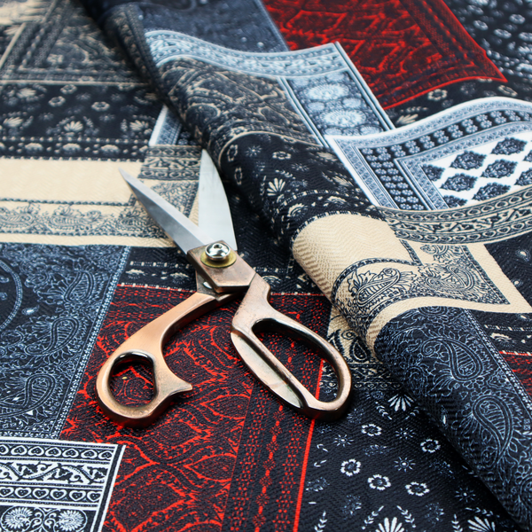A patchwork-style fabric print featuring a repetitive arrangement of square and rectangular blocks. Each block is filled with intricate navy blue, red, and cream-coloured bandana and paisley motifs, creating a dense, geometric, and traditional textile pattern.