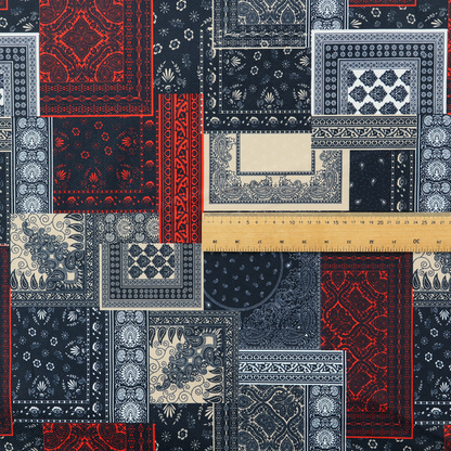 A patchwork-style fabric print featuring a repetitive arrangement of square and rectangular blocks. Each block is filled with intricate navy blue, red, and cream-coloured bandana and paisley motifs, creating a dense, geometric, and traditional textile pattern.