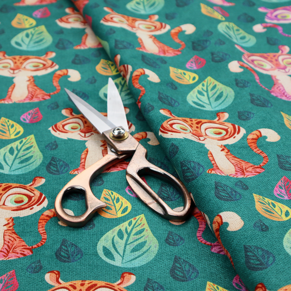 A teal fabric print featuring a whimsical, repeating pattern of cute, cartoon-style baby tigers and stylized leaves. The tigers are rendered in vibrant shades of pink, orange, and purple, while the leaves appear in varied hues, creating a playful and colourful jungle-themed aesthetic.