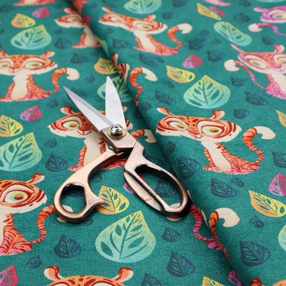 A teal fabric print featuring a whimsical, repeating pattern of cute, cartoon-style baby tigers and stylized leaves. The tigers are rendered in vibrant shades of pink, orange, and purple, while the leaves appear in varied hues, creating a playful and colourful jungle-themed aesthetic.