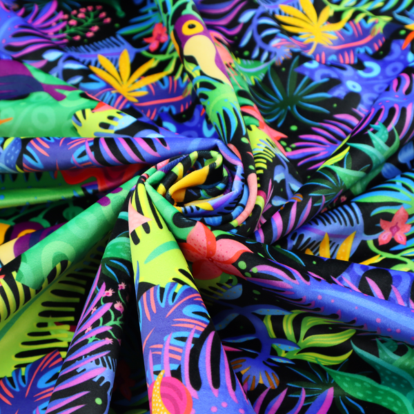A vibrant, tropical-themed fabric print featuring a dense pattern of colourful toucans, flamingos, and lush jungle leaves against a black background. The design incorporates bright neon hues of pink, purple, lime green, and yellow, creating a bold, exotic, and high-energy aesthetic.