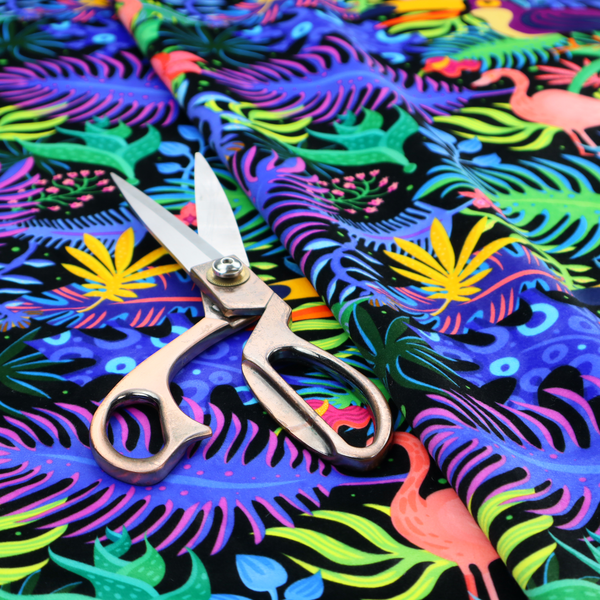A vibrant, tropical-themed fabric print featuring a dense pattern of colourful toucans, flamingos, and lush jungle leaves against a black background. The design incorporates bright neon hues of pink, purple, lime green, and yellow, creating a bold, exotic, and high-energy aesthetic.
