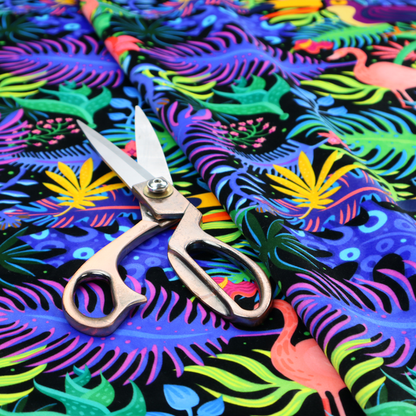 A vibrant, tropical-themed fabric print featuring a dense pattern of colourful toucans, flamingos, and lush jungle leaves against a black background. The design incorporates bright neon hues of pink, purple, lime green, and yellow, creating a bold, exotic, and high-energy aesthetic.