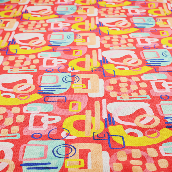 A vibrant fabric print featuring an abstract, mid-century modern design. The pattern consists of overlapping geometric shapes—circles, rectangles, and arches—in a lively palette of coral, bright yellow, teal, and soft peach on a coral-red background, creating a playful and retro aesthetic.