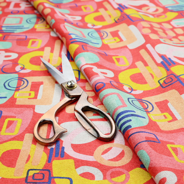 A vibrant fabric print featuring an abstract, mid-century modern design. The pattern consists of overlapping geometric shapes—circles, rectangles, and arches—in a lively palette of coral, bright yellow, teal, and soft peach on a coral-red background, creating a playful and retro aesthetic.