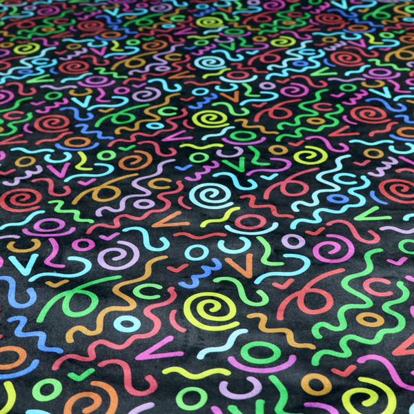 A black fabric print featuring a retro, 90s-inspired pattern of colourful, hand-drawn-style doodles. The design includes vibrant neon swirls, squiggles, and V-shapes in shades of pink, yellow, blue, orange, and green, creating a nostalgic, high-energy, and playful aesthetic.