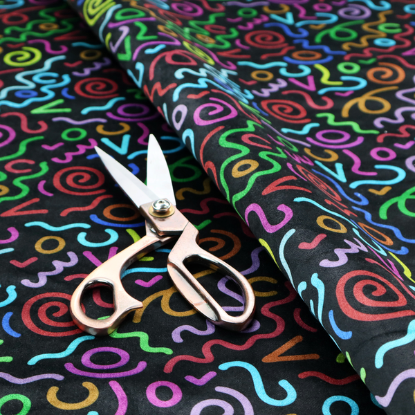 A black fabric print featuring a retro, 90s-inspired pattern of colourful, hand-drawn-style doodles. The design includes vibrant neon swirls, squiggles, and V-shapes in shades of pink, yellow, blue, orange, and green, creating a nostalgic, high-energy, and playful aesthetic.