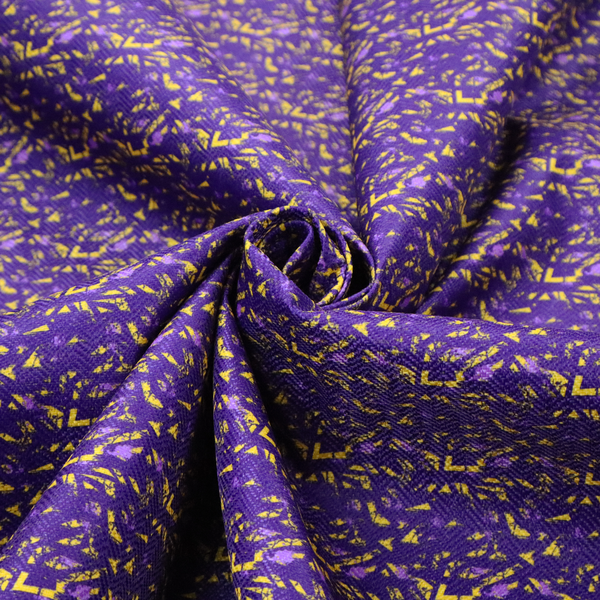 A vibrant fabric print featuring a dense, abstract pattern of bright yellow, sharp-edged shapes scattered across a deep, solid purple background. The design creates a textured, dynamic, and modern look.