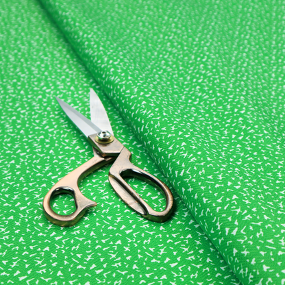 A bright, vibrant green fabric print featuring a repetitive, minimalist pattern of small, white, irregular flecks or specks. The design creates a textured, clean, and modern look.