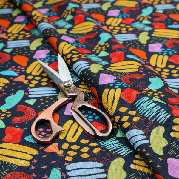 This fabric features a lively, abstract pattern set against a deep navy background. The design is filled with a dense, colourful array of hand-drawn shapes, including squiggles, small arches, and organic blobs in a vibrant palette of yellow, red, orange, teal, light blue, and purple.