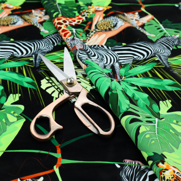 This fabric features a lush, vibrant jungle scene set against a deep black background. The pattern is filled with a dense variety of tropical foliage, including large monstera and palm leaves in multiple shades of green.