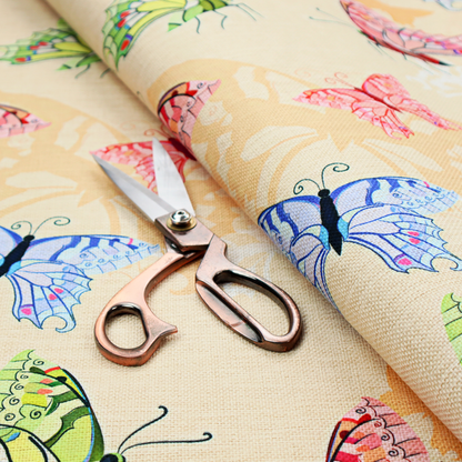 This fabric features a whimsical, repeating pattern of colourful butterflies scattered across a light beige, textured background. The butterflies are rendered in various sizes and a vibrant colour palette, including shades of pink, purple, lime green, and soft blue, with delicate black wing detailing.
