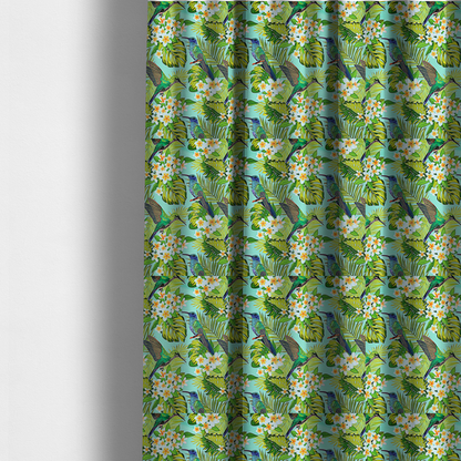 The fabric used to create these made-to-measure curtains is a fabric features a vibrant, tropical pattern set against a bright turquoise background. The design showcases hummingbirds in various poses—some perched and others in flight—surrounded by clusters of white plumeria flowers and lush, layered palm and monstera leaves in shades of green and yellow.
