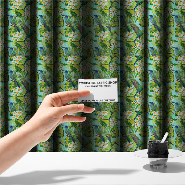 The fabric used to create these made-to-measure curtains is a fabric features a vibrant, tropical pattern set against a bright turquoise background. The design showcases hummingbirds in various poses—some perched and others in flight—surrounded by clusters of white plumeria flowers and lush, layered palm and monstera leaves in shades of green and yellow.