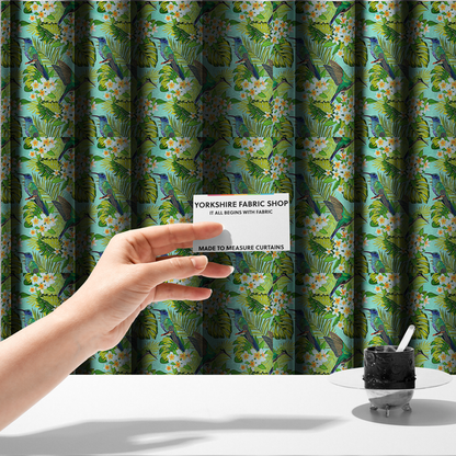 The fabric used to create these made-to-measure curtains is a fabric features a vibrant, tropical pattern set against a bright turquoise background. The design showcases hummingbirds in various poses—some perched and others in flight—surrounded by clusters of white plumeria flowers and lush, layered palm and monstera leaves in shades of green and yellow.