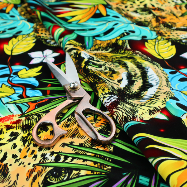 This fabric features a bold, artistic jungle-themed pattern set against a dark black background. The design is a dense, repeating collage of wildlife portraits, featuring alternating heads of leopards and tigers with intense, detailed expressions.