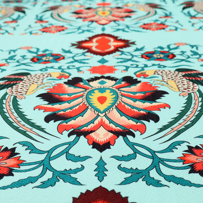 This fabric features an intricate, symmetrical folk-art inspired pattern set against a soft, light turquoise background. The design showcases stylized birds facing toward central, ornate floral bursts, rendered in a bold colour palette of vibrant red, deep orange, teal, and charcoal.