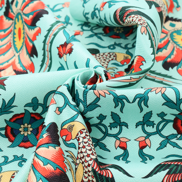 This fabric features an intricate, symmetrical folk-art inspired pattern set against a soft, light turquoise background. The design showcases stylized birds facing toward central, ornate floral bursts, rendered in a bold colour palette of vibrant red, deep orange, teal, and charcoal.