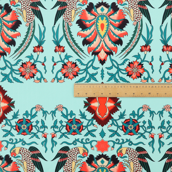 This fabric features an intricate, symmetrical folk-art inspired pattern set against a soft, light turquoise background. The design showcases stylized birds facing toward central, ornate floral bursts, rendered in a bold colour palette of vibrant red, deep orange, teal, and charcoal.