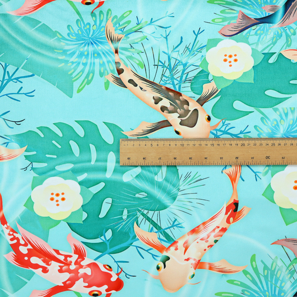 Patterned fabric featuring vibrant orange, white, and dark blue koi fish swimming among lush tropical monstera leaves, water ripples, and white flowers on a light teal background.