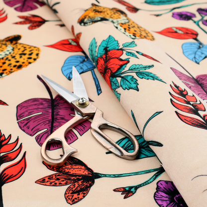 Patterned fabric featuring a repeating design of tiger and leopard heads interspersed with vibrant tropical flowers, orchids, and palm leaves on a cream background.