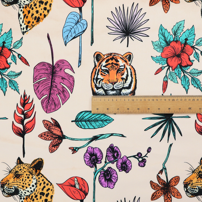 Patterned fabric featuring a repeating design of tiger and leopard heads interspersed with vibrant tropical flowers, orchids, and palm leaves on a cream background.