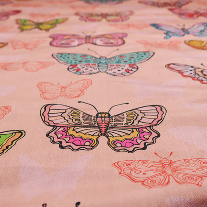 Patterned fabric featuring a whimsical, repeating design of colourful butterflies in various patterns and shades—including orange, teal, pink, and yellow—scattered among faint, outline-style butterfly silhouettes on a soft, dusty pink background.