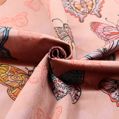 Patterned fabric featuring a whimsical, repeating design of colourful butterflies in various patterns and shades—including orange, teal, pink, and yellow—scattered among faint, outline-style butterfly silhouettes on a soft, dusty pink background.
