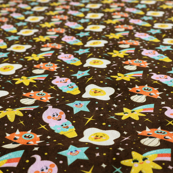 A whimsical, repeating fabric pattern featuring cartoon-style fried eggs, happy ice cream cones, shooting stars, and colourful stars on a dark chocolate brown background.