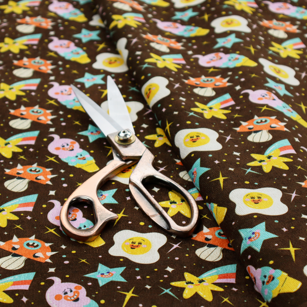 A whimsical, repeating fabric pattern featuring cartoon-style fried eggs, happy ice cream cones, shooting stars, and colourful stars on a dark chocolate brown background.