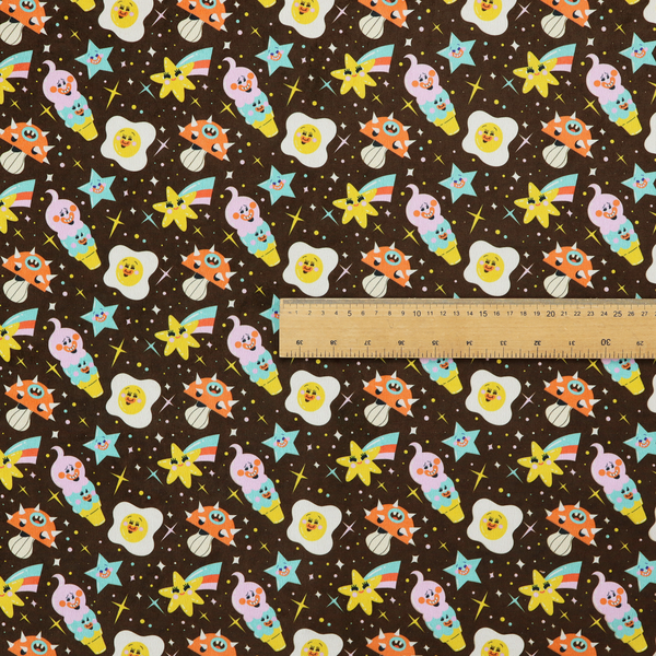 A whimsical, repeating fabric pattern featuring cartoon-style fried eggs, happy ice cream cones, shooting stars, and colourful stars on a dark chocolate brown background.