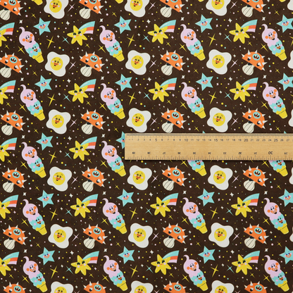 A whimsical, repeating fabric pattern featuring cartoon-style fried eggs, happy ice cream cones, shooting stars, and colourful stars on a dark chocolate brown background.
