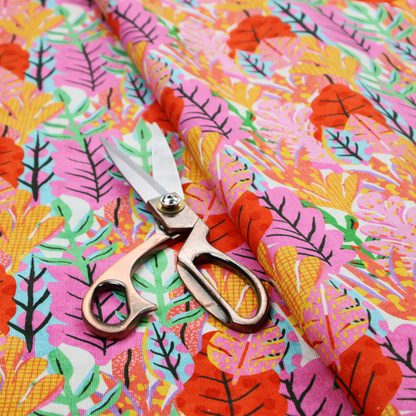 A vibrant, repeating textile pattern featuring a dense arrangement of stylized tropical leaves in saturated shades of pink, orange, yellow, and bright green against a white background.
