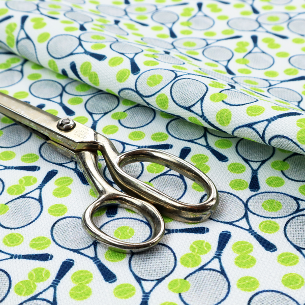 A white fabric featuring a vibrant, repeating pattern of tennis rackets and tennis balls.