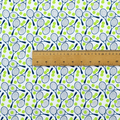 A white fabric featuring a vibrant, repeating pattern of tennis rackets and tennis balls.